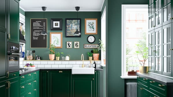Dapur berwarna hijau dengan sink berwarna putih yang mempunyai bahagian hadapan yang boleh dilihat, paip berwarna loyang, hob gas dan dua lampu siling berwarna hitam.