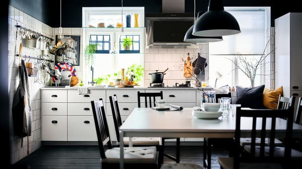Dapur berwarna hitam dan putih yang mempunyai kabinet METOD dengan kelengkapan dalaman MAXIMERA berwarna putih dan ruang makan yang mempunyai dua meja MELLTORP berwarna putih.