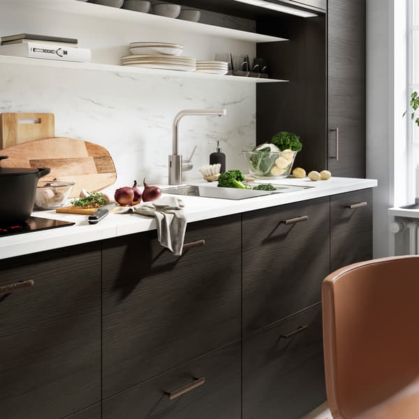 Dapur dengan panel dinding dan permukaan atas kerja kesan marmar putih, bahagian hadapan dapur kesan kayu ash berwarna coklat gelap dan pemegang berwarna hitam.