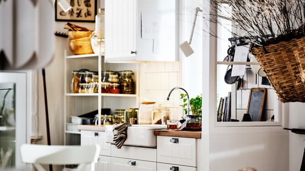Dapur gaya desa berwarna putih dengan bahagian hadapan STENSUND pada kabinet METOD, sink berwarna putih dan para-para dengan balang dan perkakas.
