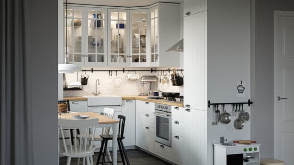 Dapur gaya tradisional dengan bahagian hadapan dan kabinet berwarna putih dengan pintu kaca, meja makan, kerusi dan dapur mainan.