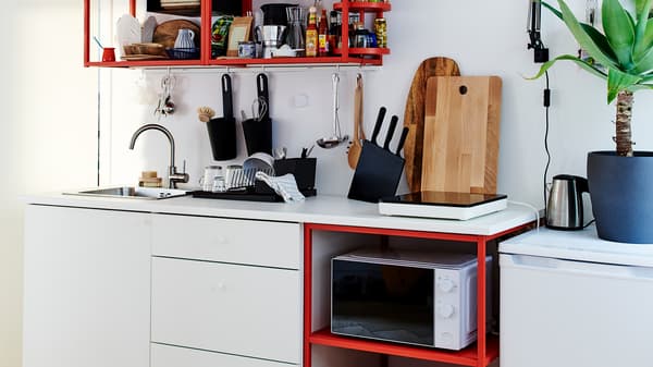Dapur kecil berwarna merah/putih yang mempunyai hob aruhan mudah alih, landas cencang kayu dan pengetus pinggan berwarna hitam.