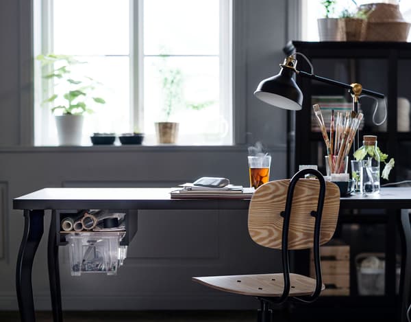 Dark coloured desk with work lamp facing a window