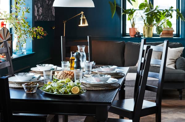 Dark dining room with black dining table and chairs. Table is set with white dishes and round placemats.
