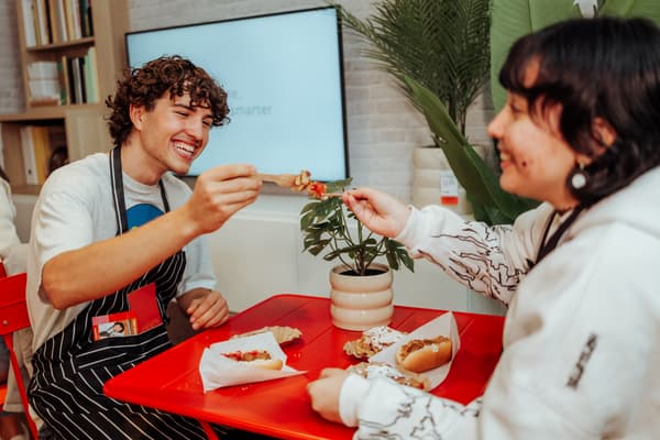 Das Bild zeigt 2 Personen, die mit dem IKEA Hotdog anstoßen.