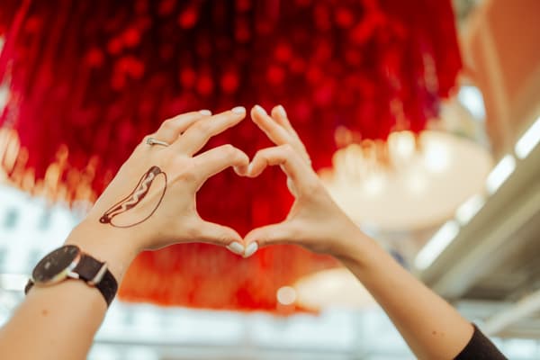 Das Bild zeigt ein Herz geformt mit zwei Händen mit einem IKEA Hotdog Tattoo.