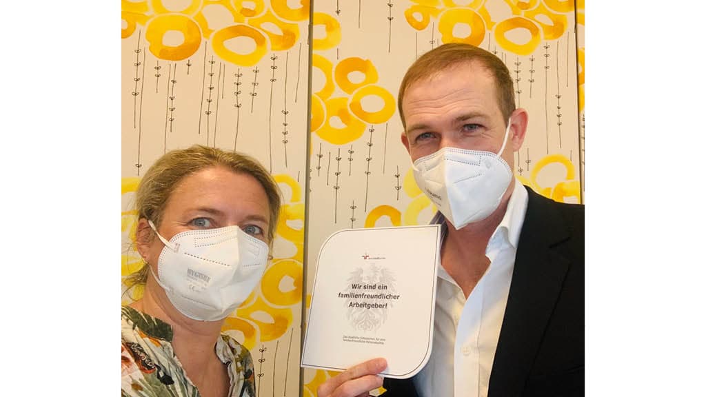 Das Bild zeigt zwei Personen mit FFP2-Masken, die gemeinsam ein Zertifikat oder eine Auszeichnung halten. Auf dem Dokument steht:
„Wir sind ein familienfreundlicher Arbeitgeber!“
Der Hintergrund mit dem gelben, floralen Muster deutet ebenfalls auf eine IKEA-Filiale hin.