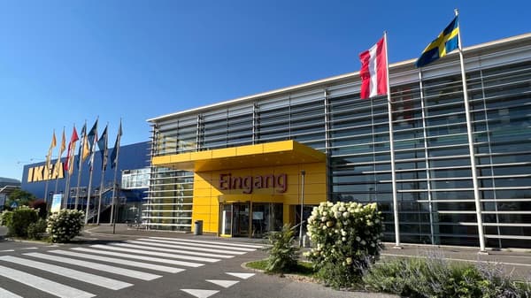 Das Eingangsportal von IKEA Graz bei strahlendem Sonnenschein mit blauem Himmel und wehenden Flaggen.