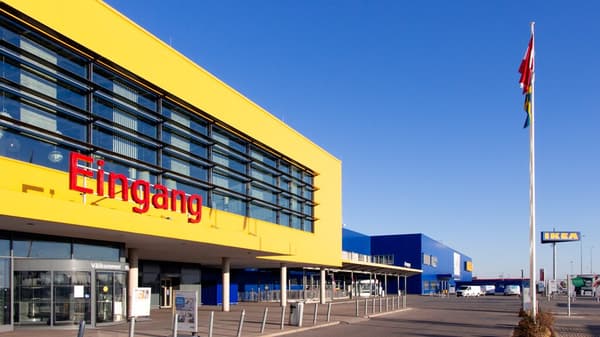 Das Eingangsportal von IKEA Wien Nord bei strahlendem Sonnenschein mit blauem Himmel und wehenden Flaggen.