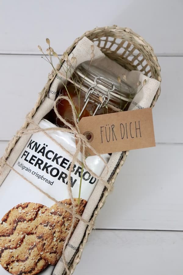 Das PENNFISK Brotkörbchen fertig befüllt mit einer VÅRARV Serviette und einem IKEA KNÄCKEBRÖD in der Mitte sowie einem kleinen Einmachglas mit Marmelade. EIne Naturfarbende Schnur und ein Geschenkanhänger mit der Aufschrift 