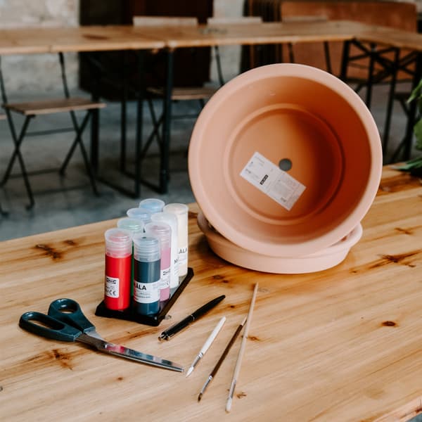 De la peinture et des pinceaux posés sur une table en bois à côté d'un cache pot en terre cuite.