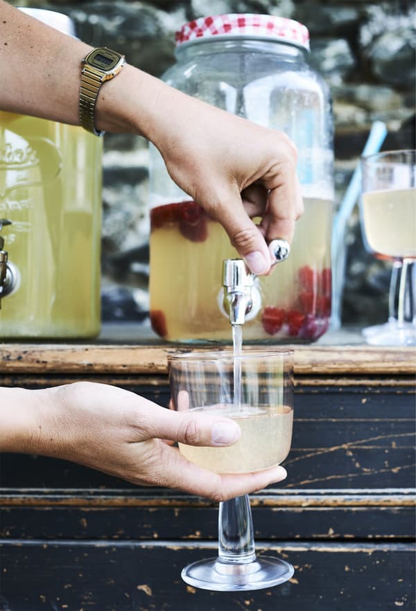 Decanting a drink into a glass from a jar with a tap.