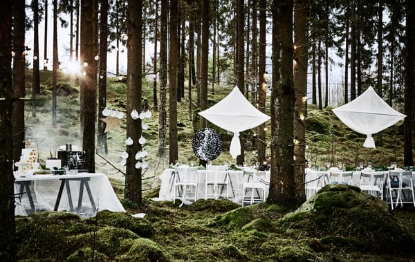 Décor de repas de noces en forêt, avec longue table blanche, chaises blanches, décorations suspendues et table à gâteau