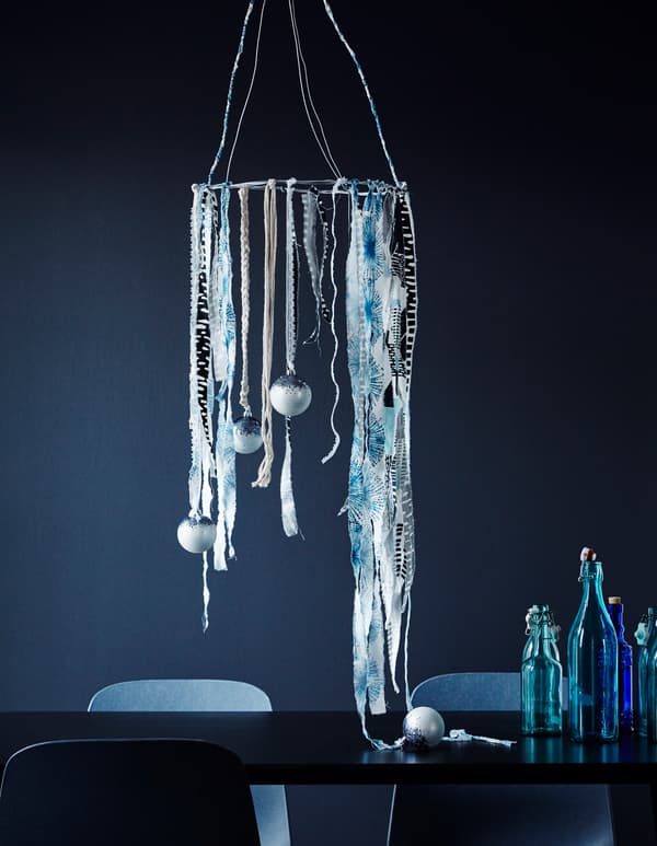 Decoración feita con tiras de teas azuis e brancas e adornos colgados dun arame circular suspendido sobre unha mesa.