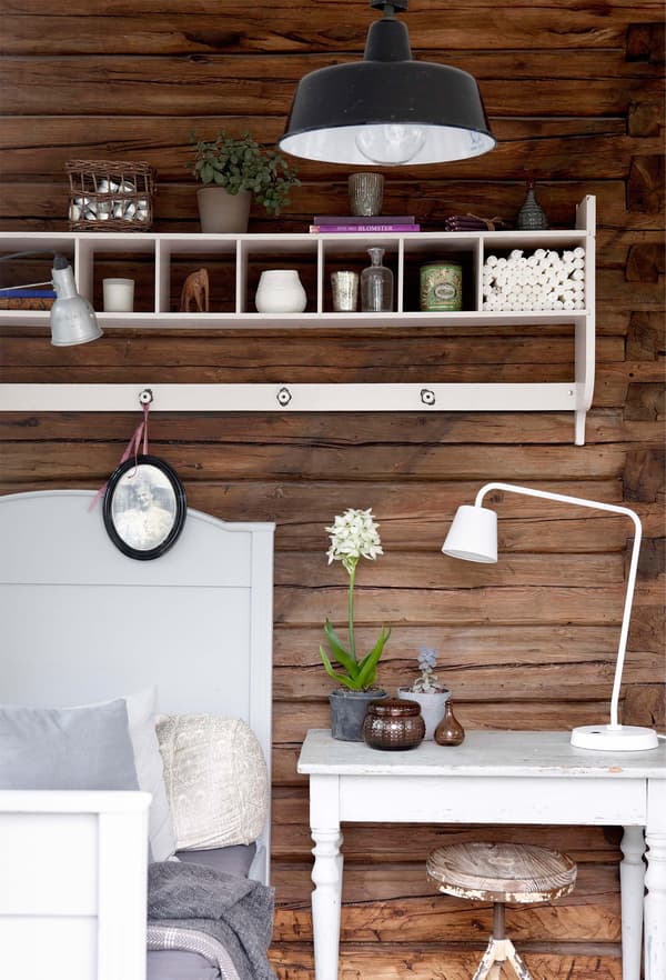 Decoración rústica con la pared de madera teñida de color oscuro es un fondo muy vistoso para los muebles blancos del dormitorio.