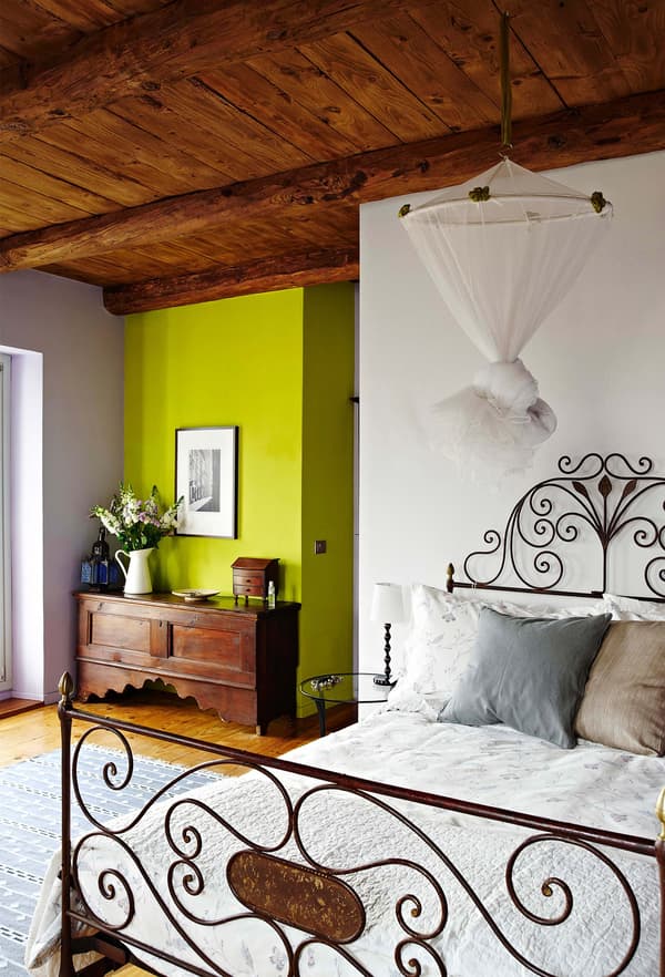 Decoración rústica con una estructura de cama de hierro forjado en un dormitorio con techo de madera.