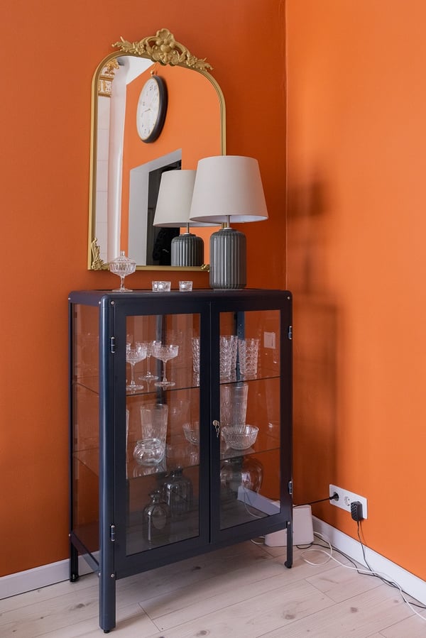 Decorative cabinet detail with glassware, table lamps, and vintage-style mirror on orange wall