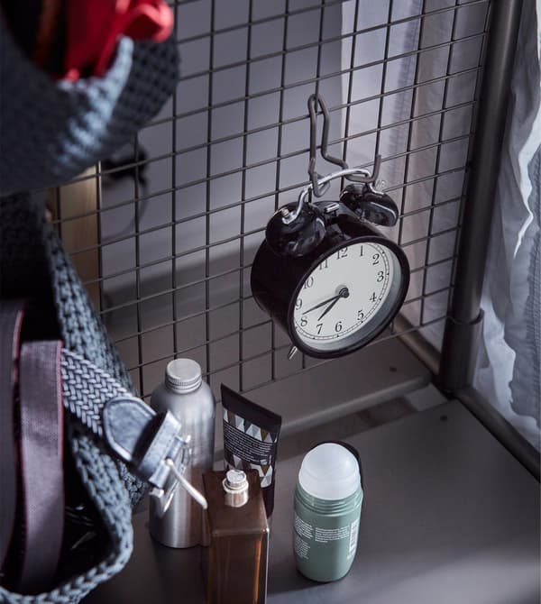 DEKAD alarm clock in black steel, hanging on the hook of a mesh steel room divider.