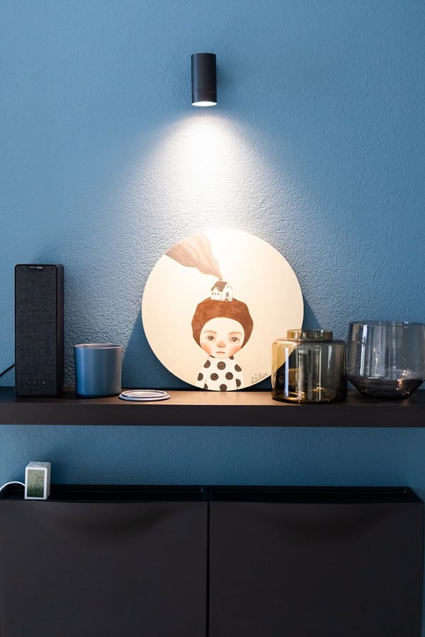 Декоративная полка с предметами искусства, свечами и акцентным освещением на синей стене спальни