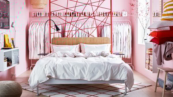 DELAKTIG bed on a red and white SIMESTED rug in the middle of a bedroom with pink walls, racks of clothes against the wall.