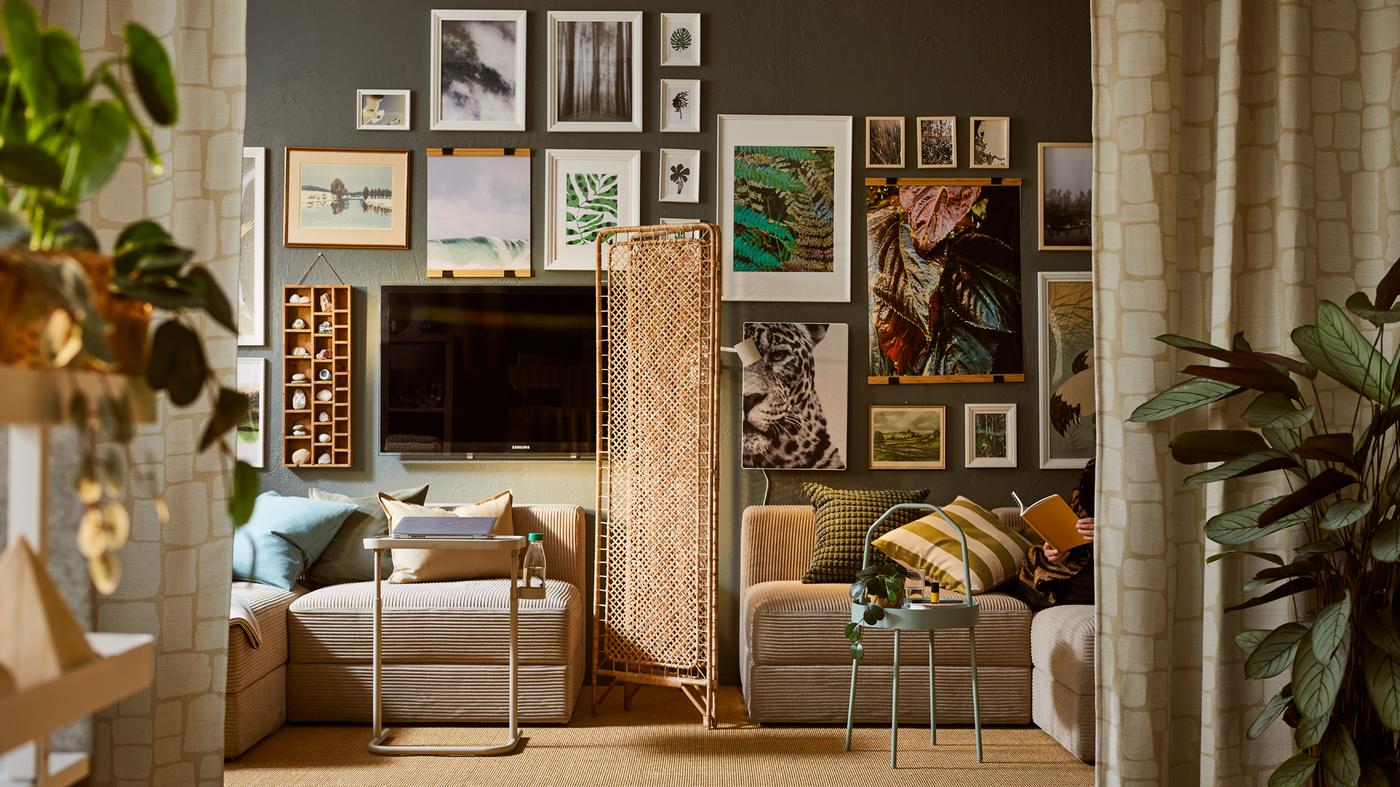 Deler av en JÄTTEBO sofa på hver sin side av en TOLKNING romavdeler av rotting, ved en vegg full av innrammet kunst.