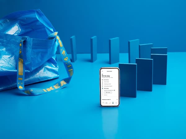 Delle tessere da domino blu delle dimensioni di uno smartphone sono allineate accanto a una borsa FRAKTA blu di IKEA. Quella davanti è uno smartphone acceso.