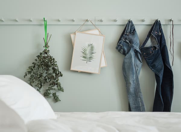 Denims, fleurs séchées et œuvres d’art accrochés à des patères peintes de la même couleur que le mur
