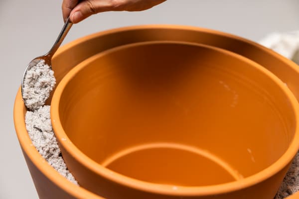 Der kleine Tontopf wird nun in den Großen gestellt. Der Abstand zwischen den Töpfen wird mithilfe eines Löffels mit Sand befüllt. 
