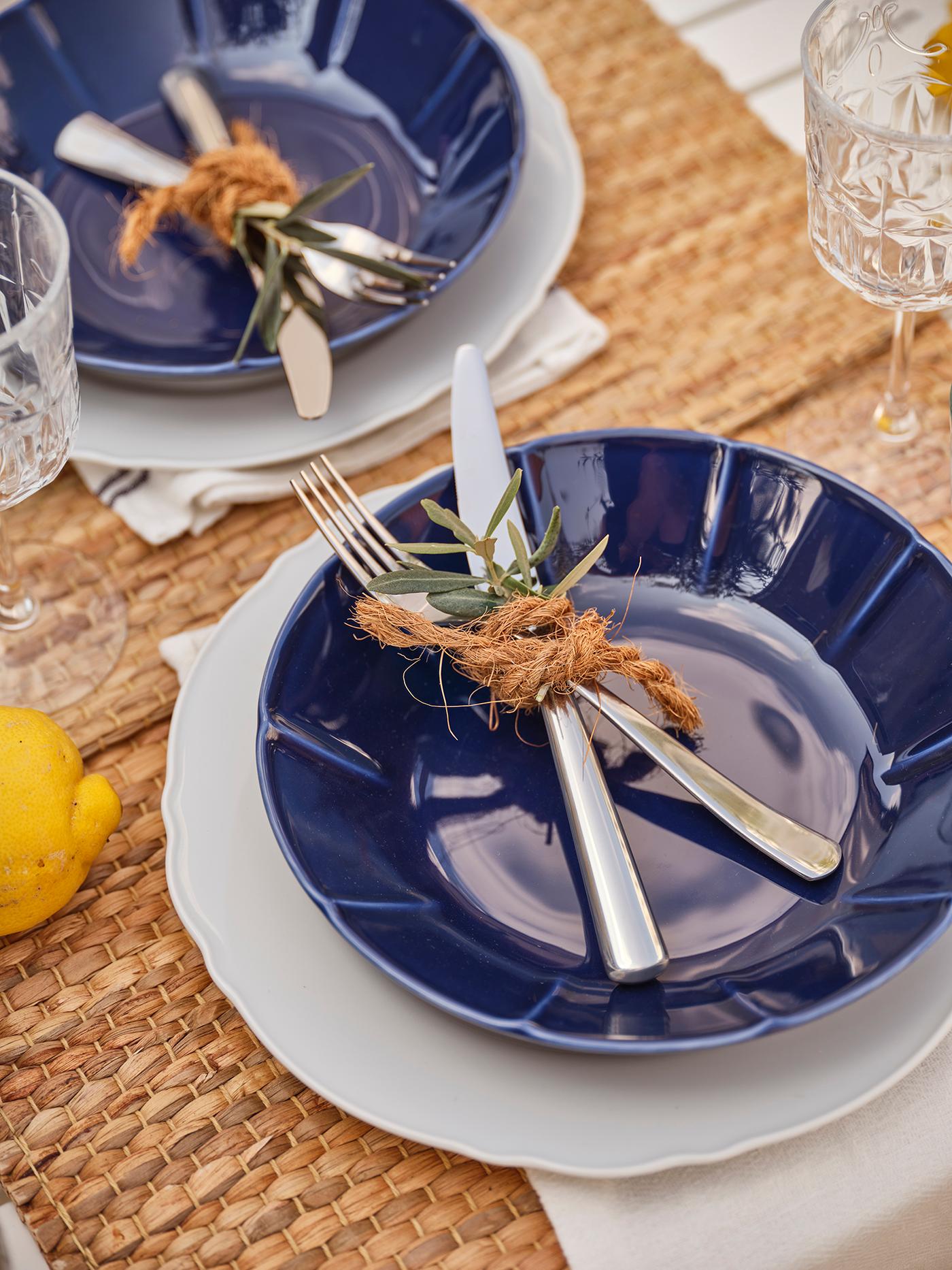 Des assiettes bleues avec des couverts liés par une corde de noix de coco.