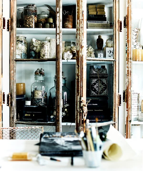 Des bocaux et des livres rangés dans une armoire à portes vitrées avec des portes rustiques.