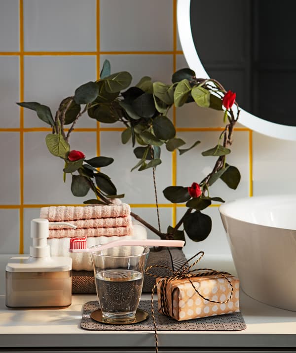 Des branches de feuilles artificielles vertes IKEA SMYCKA en forme de cœur décorent une étagère de salle de bain.