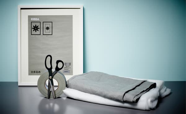 Des ciseaux, du ruban adhésif, un cadre, du tissu gris et de l’ouate blanche sur une table. Ils seront utilisés pour réaliser un mur insonorisé.