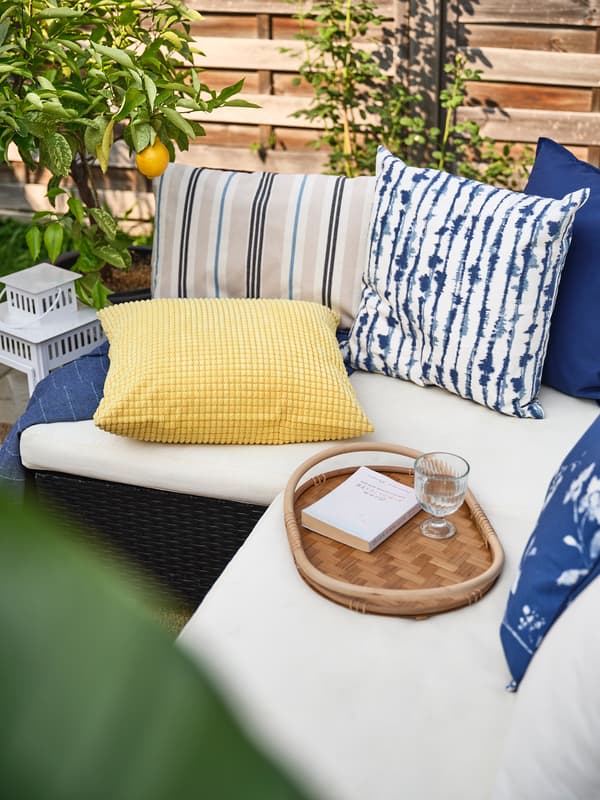 Des coussins bleus et jaunes posés sur un canapé d'extérieur beige.
