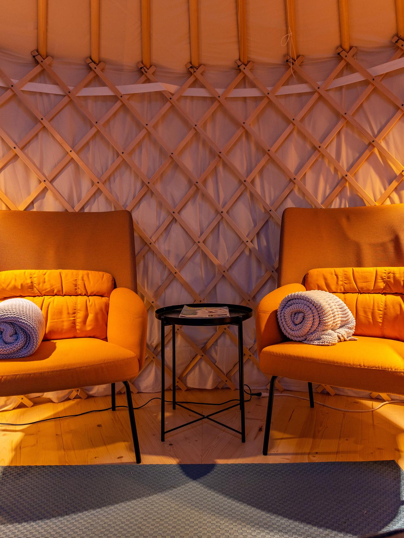 Des fauteuils avec un dossier haut ainsi que chacun une couverture enroulée se trouvent devant la cloison d’une yourte