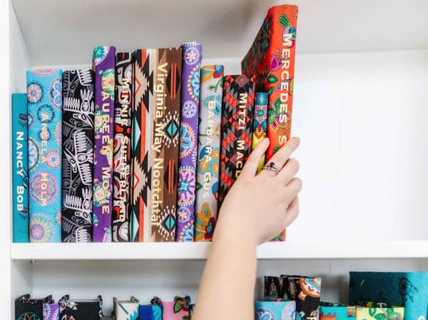 Des livres placés à la main dans une bibliothèque. Les livres sont recouverts de tissu et portent un nom imprimé en doré sur l’épine.