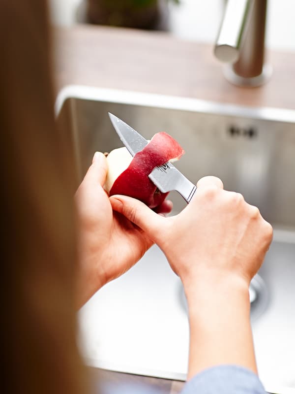Des mains épluchent une pomme rouge avec un couteau à éplucher en acier inoxydable.