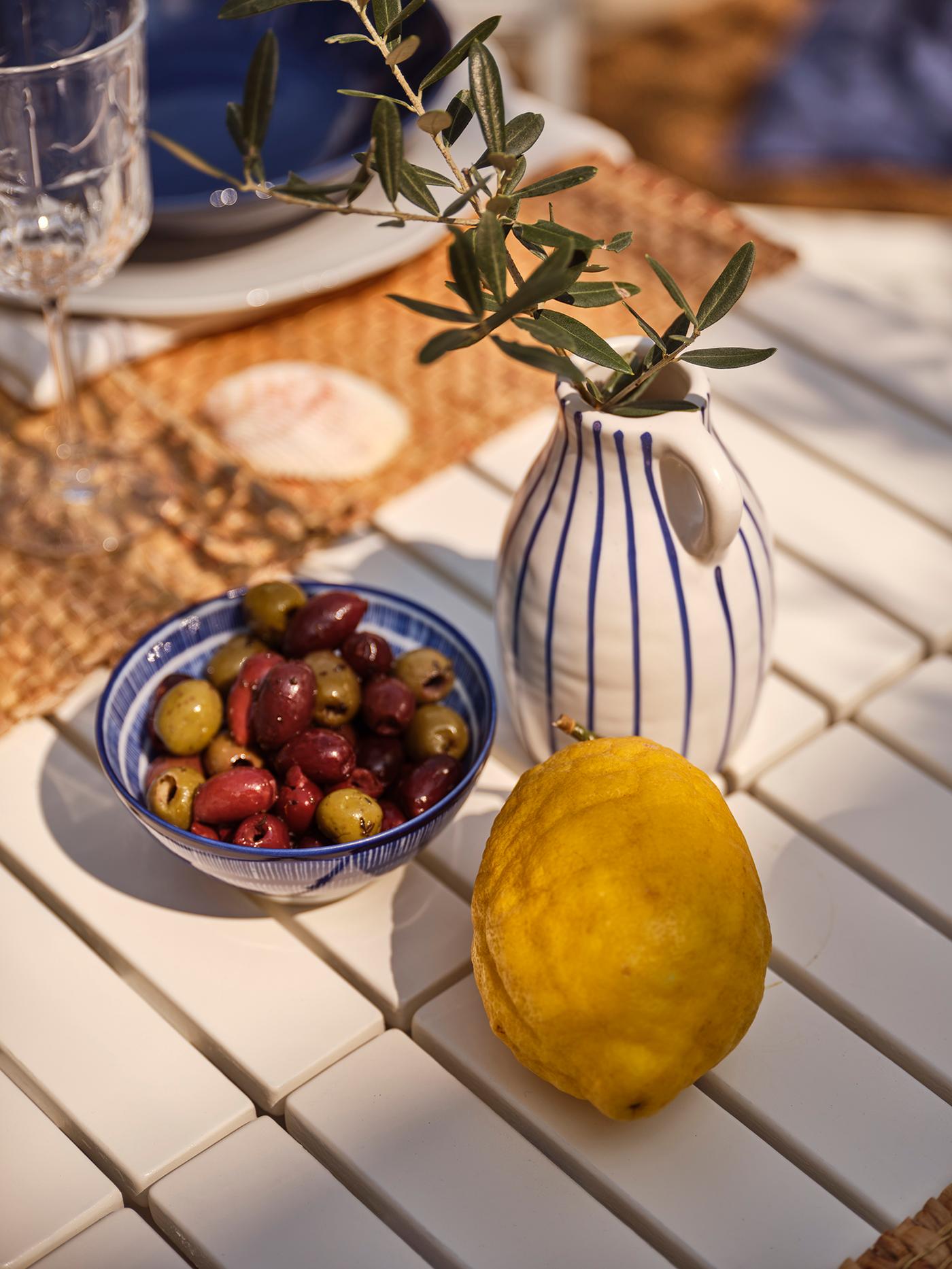 Des olives et un citron sur une table blanche, au soleil.