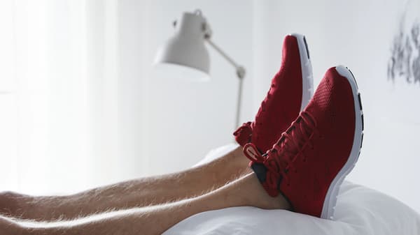 Des pieds portant des baskets rouge vif posés sur un tas d’oreillers blancs.