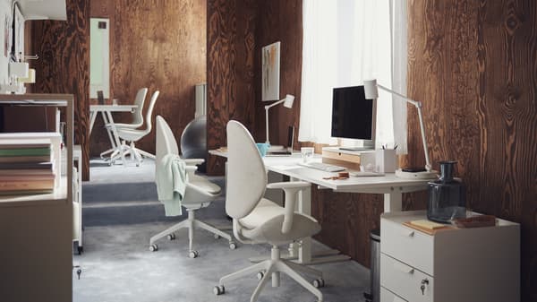Des postes de travail comprenant des bureaux TROTTEN blancs et des chaises de bureau HATTEFJÄLL et LÅNGFJÄLL, dans un bureau avec du tapis et des murs de lambris brun.