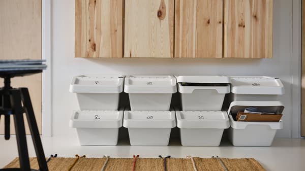 Des rangées de poubelles avec couvercle SORTERA blanches empilées sous des armoires en pin, accompagnées d’un tapis.