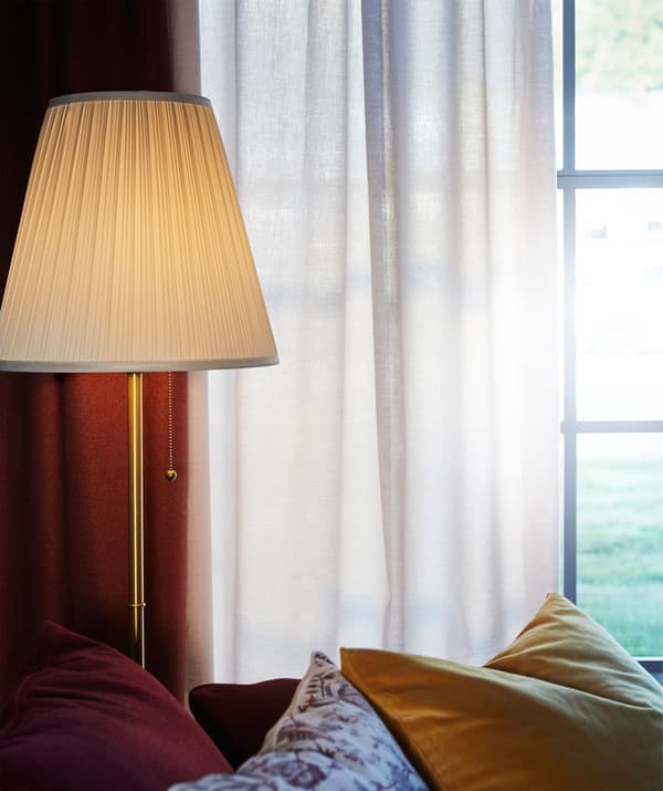 Des rideaux en coton TIBAST et une lampe devant la fenêtre d’un séjour.