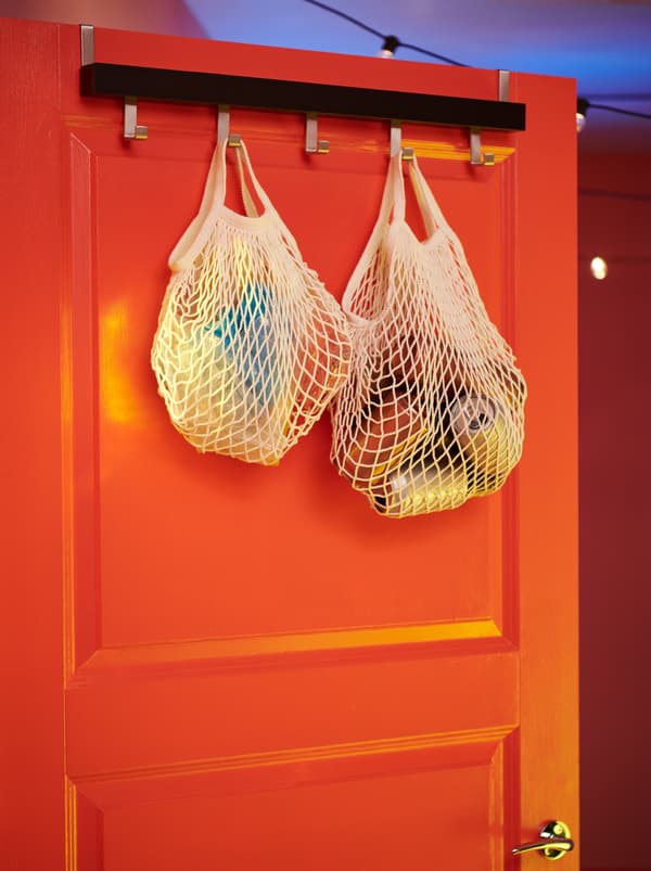 Des sacs filets KUNGSFORS remplis de canettes vides et autres déchets, suspendus à une patère TJUSIG montée au-dessus d’une porte.