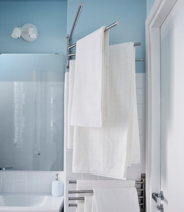 Des serviettes blanches sont suspendues à un porte-serviettes qui pivote vers l’intérieur et l’extérieur du mur dans cette petite salle de bain.