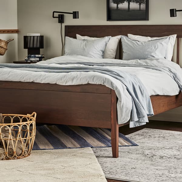 Des tapis VRENSTED, VEDBÄK et TVERSTED sous un lit brun foncé fait avec un linge de lit à rayures bleues et un jeté bleu clair.