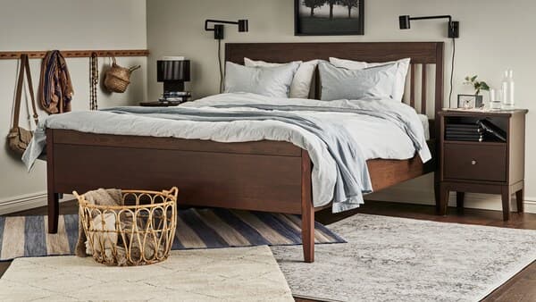 Des tapis VRENSTED, VEDBÄK et TVERSTED sous un lit brun foncé IDANÄS fait avec un linge de lit à rayures bleues BERGPALM et un jeté gris.