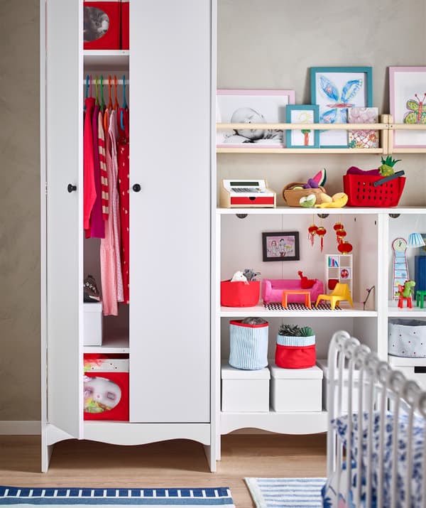 Des vêtements et des boîtes rouges dans une grande garde-robe, des livres des jouets et des boîtes sur des étagères ouvertes.