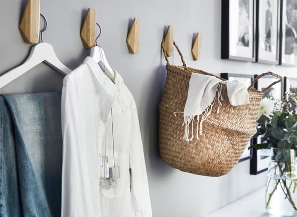 Des vêtements et un panier suspendus à des crochets en bois sur un mur gris.