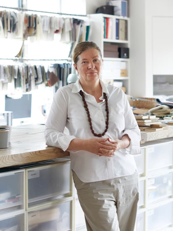 Designerin Ilse Crawford lehnt mit einer weißen Bluse und einer beigefarbenen Hose bekleidet an einer Arbeitsfläche in ihrem Studio.