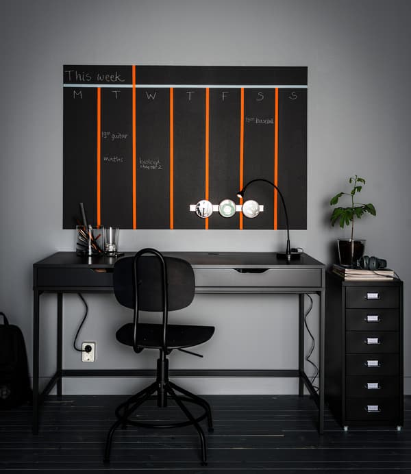 Desk organization ideas like drawer inserts, magnetic containers and a painted wall calendar shown in and above a grey desk with two drawers.