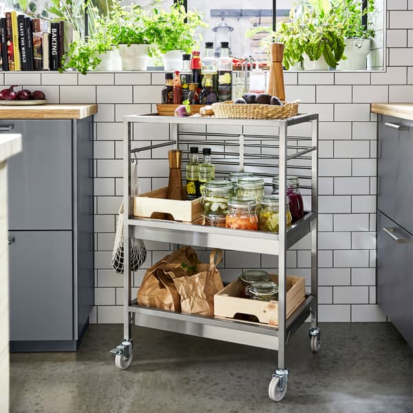 Desserte inox sur roulettes, près d’une fenêtre. Elle accueille des bouteilles d’huile, des avocats et des légumes marinés.